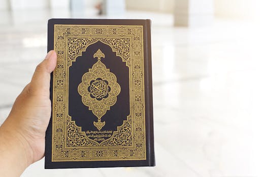 A close-up of a Quran with gold Arabic calligraphy held in hand, symbolizing faith and spirituality.