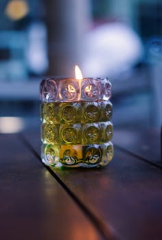 Warm candlelight in a decorative glass holder creates a cozy ambiance on a table, perfect for relaxation.