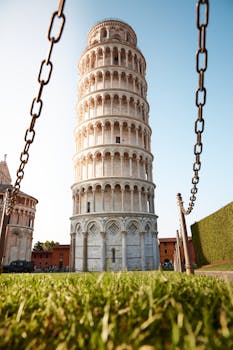 Iconic Leaning Tower of Pisa, bathed in sunlight, surrounded by lush greenery.